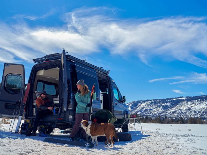 Couple and their dog beside a camper van in the mountains